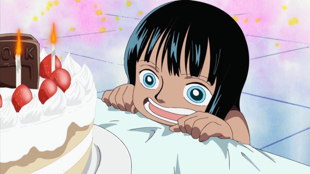 Una giovane Nico Robin in One Piece davanti a una torta di compleanno